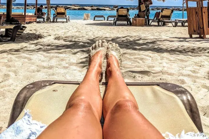 The view from a sun lounger on white sand: palm-thatch parasols, empty loungers and calm blue sea